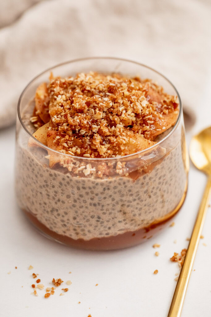 Close up of a cup of chia pudding topped with sauteed apples and date crumble.