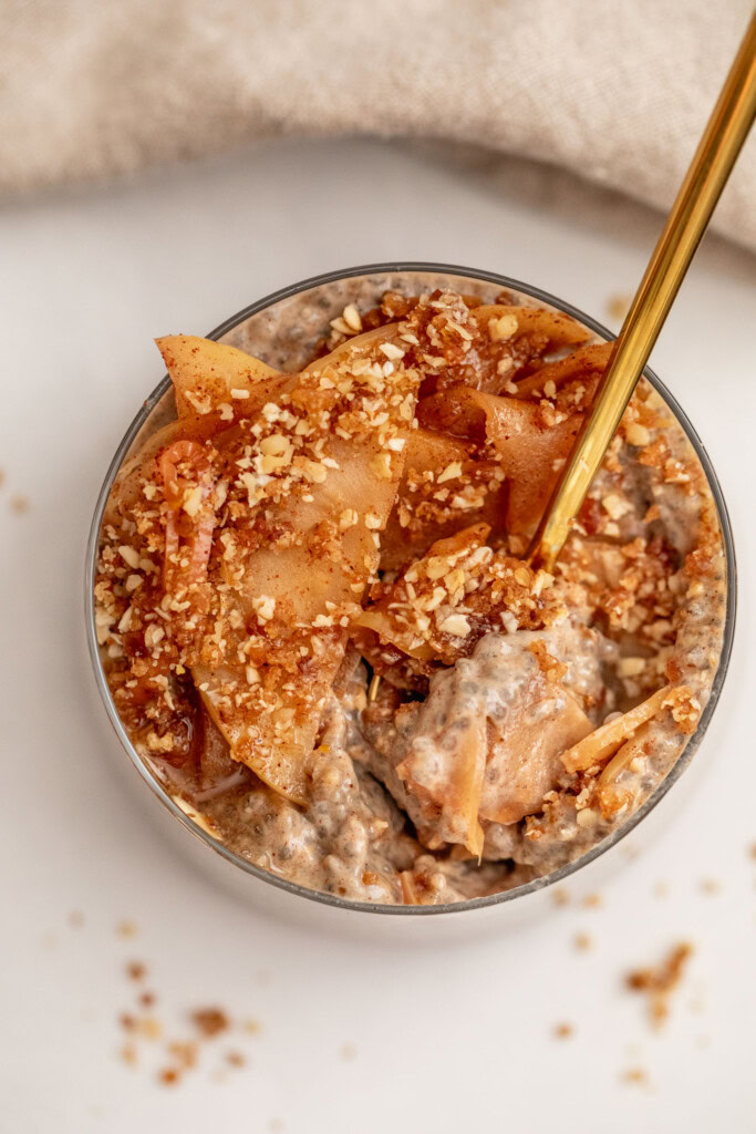 Gold spoon digging into the top of the date crumble and sauteed apples to get to the chia pudding layer.