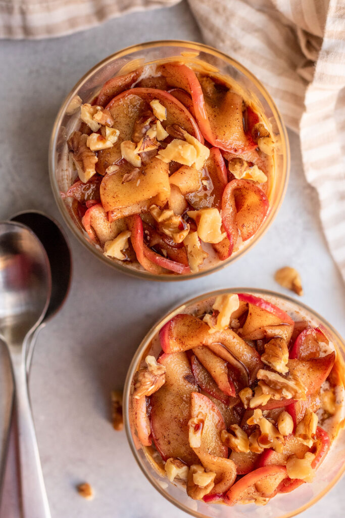 Top down view of two jars of overnight oats topped with sauteed apples and walnut pieces.