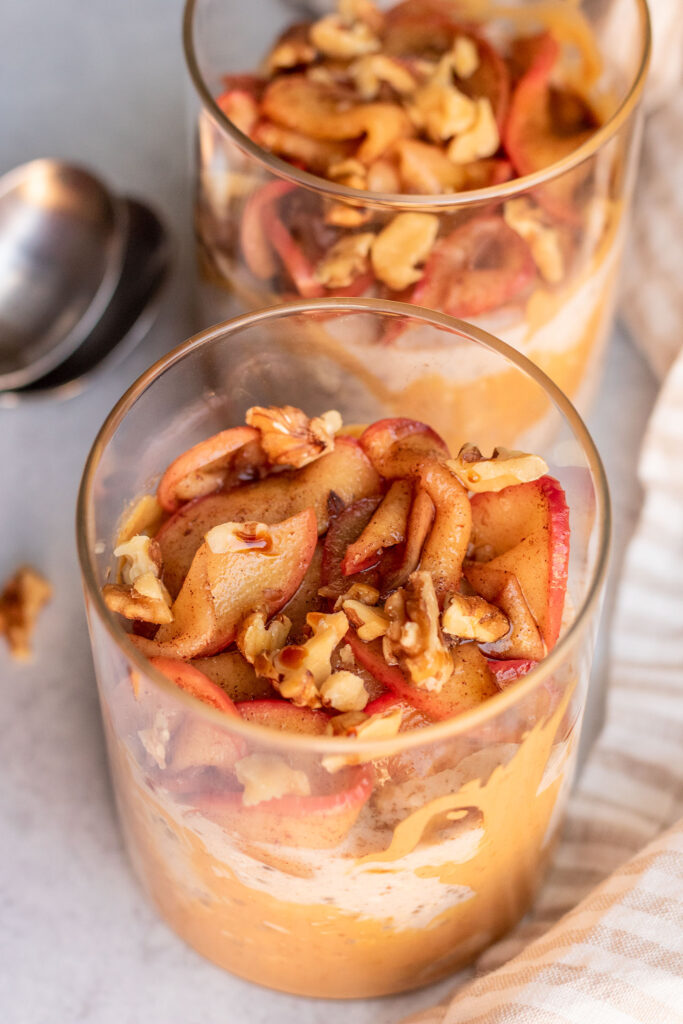 Side view of 2 jars of overnight oats topped with sauteed apples and walnuts with two spoons set to the side.