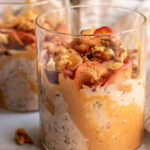 Peanut butter smeared jar filled with apple pie overnight oats topped with sauteed apples and walnuts.