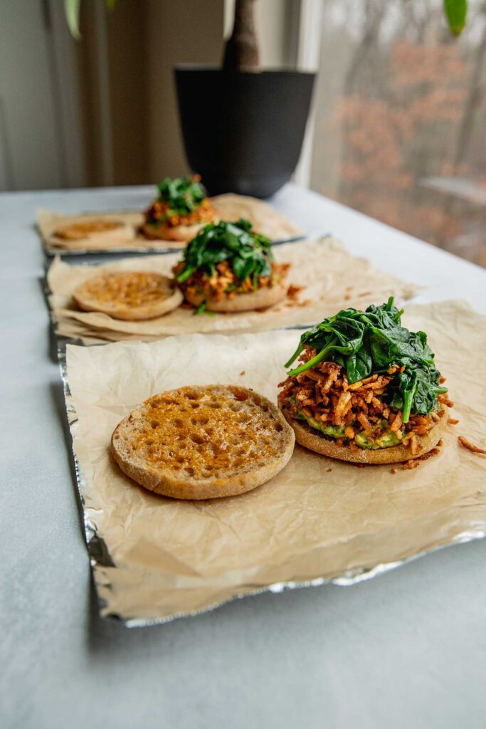 Partially assembled breakfast sandwiches lined up over parchment paper and foil.