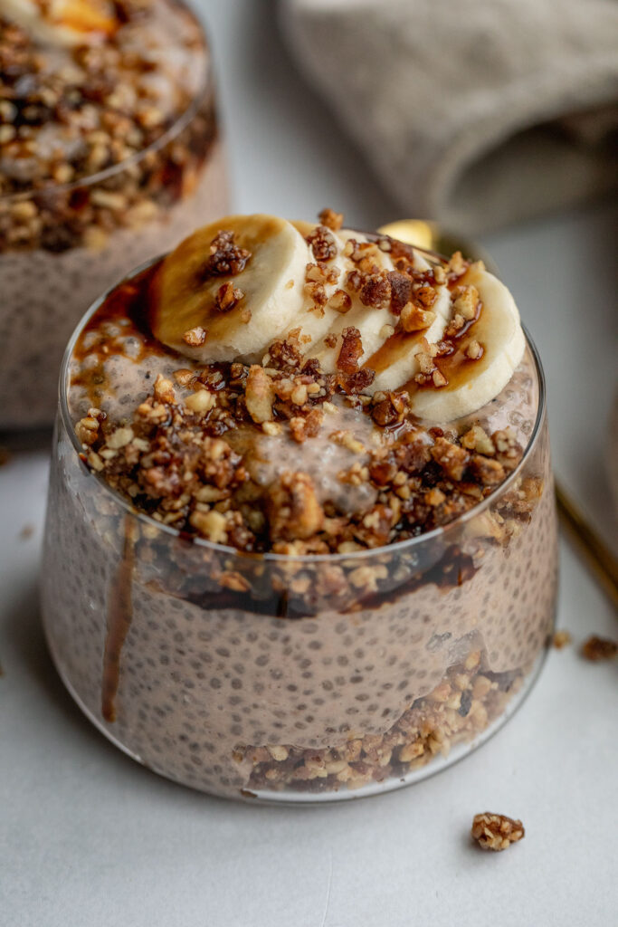 Jar of chia pudding layered with date pecan crumble, banana slices and topped with date syrup.