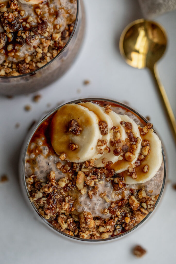 Close up of the top of a chia seed pudding topped with banana slices, pecan crumble and date syrup.