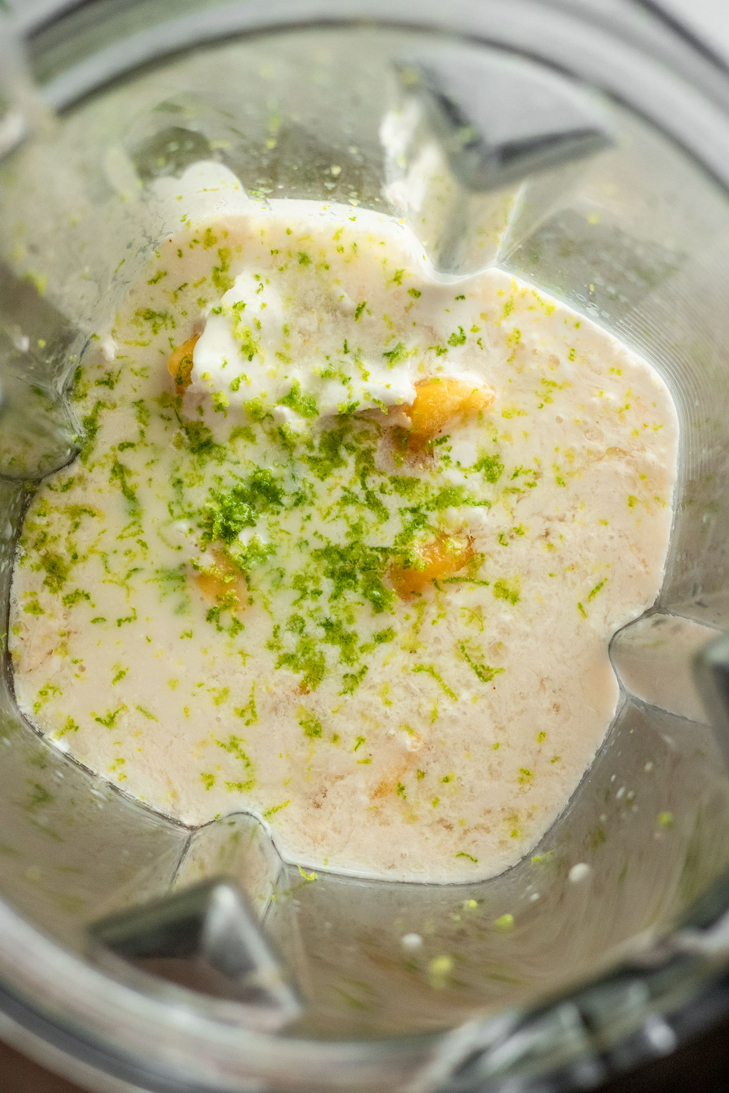 Blending coconut milk, mango, lime juice, and sweetener together in a blender.
