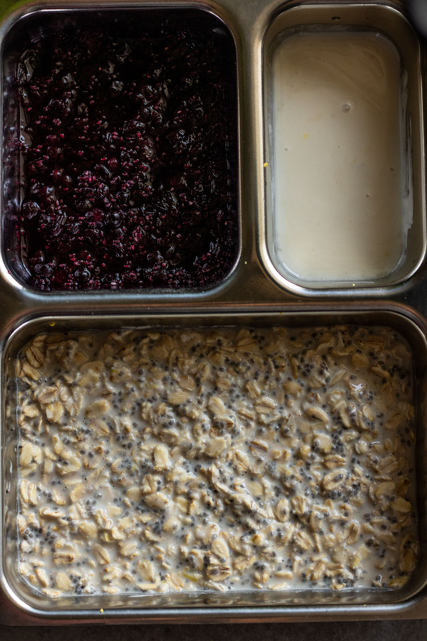 Preparing the overnight oats and toppings in a breakfast box container. Oats, chia jam and lemon yogurt all prepped in separate sections.