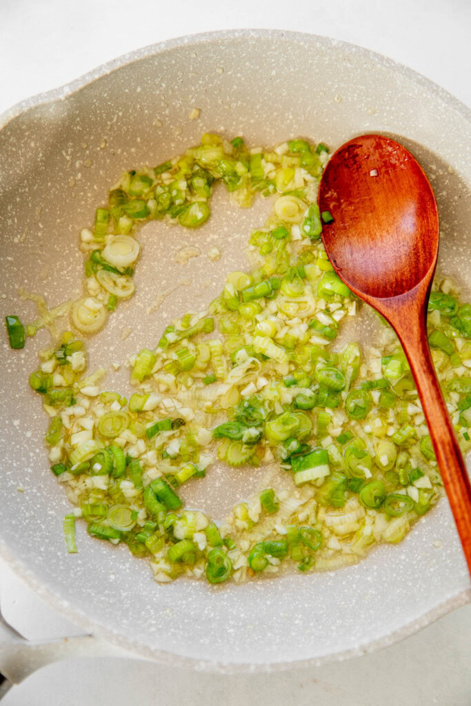 Cooking scallions and garlic being sautéed in oil in a pan.