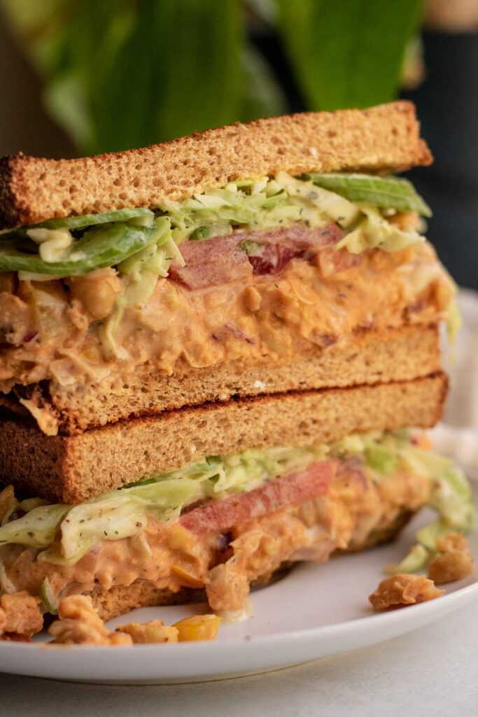 Close up side view of the inside of a sandwich cut in half stacked with chickpea salad and slaw.