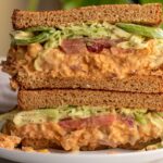 Chickpea salad sandwich stacked together on a plate filled with chickpea salad and tahini slaw.
