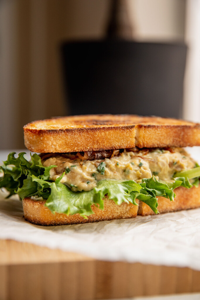 Fully assembled chickpea salad sandwich with caramelized onions on top of parchment paper.