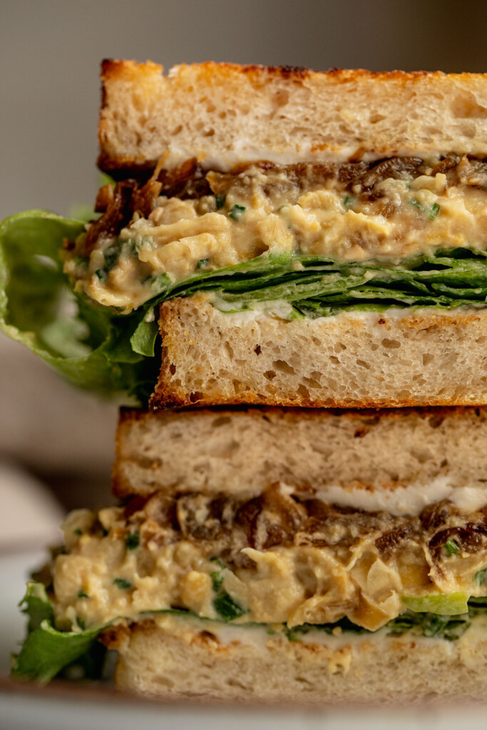 Sandwich stuffed with caramelized onion chickpea salad, lettuce and more caramelized onion cut in half and stacked on top of each other.