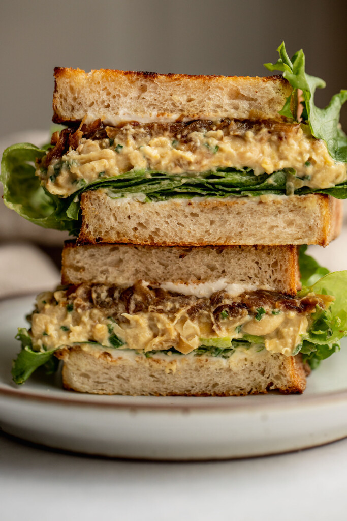 Sandwich cut in half showing a layer of cream cheese, lettuce, chickpea salad, and caramelized onion.