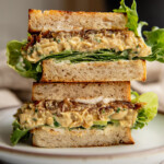 Sandwich cut in half and stacked on top of each other showing layers of lettuce, cream cheese, chickpea salad and caramelized onions.
