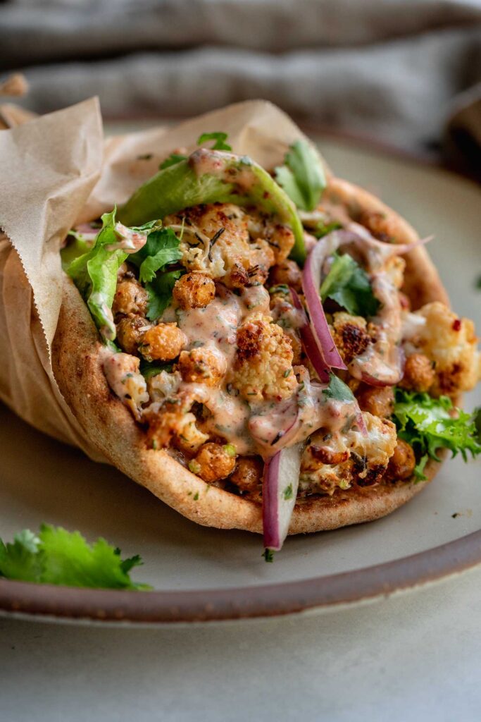 Plate with a cauliflower and chickpea wrap stuffed with lettuce, pickled onions and chipotle sauce.