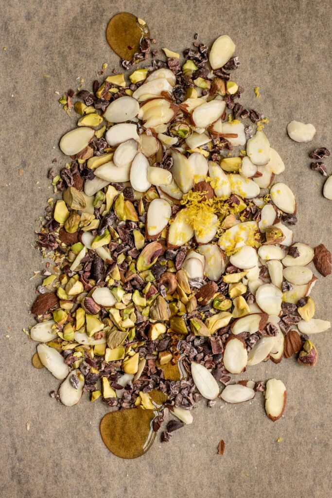 Combining the nuts with lemon zest and maple syrup on a baking tray.