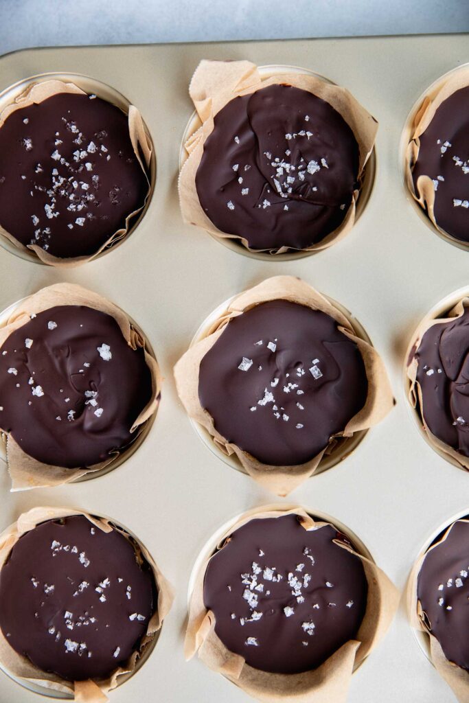 Oat cups layered with dark chocolate and flaky salt in a muffin tin.
