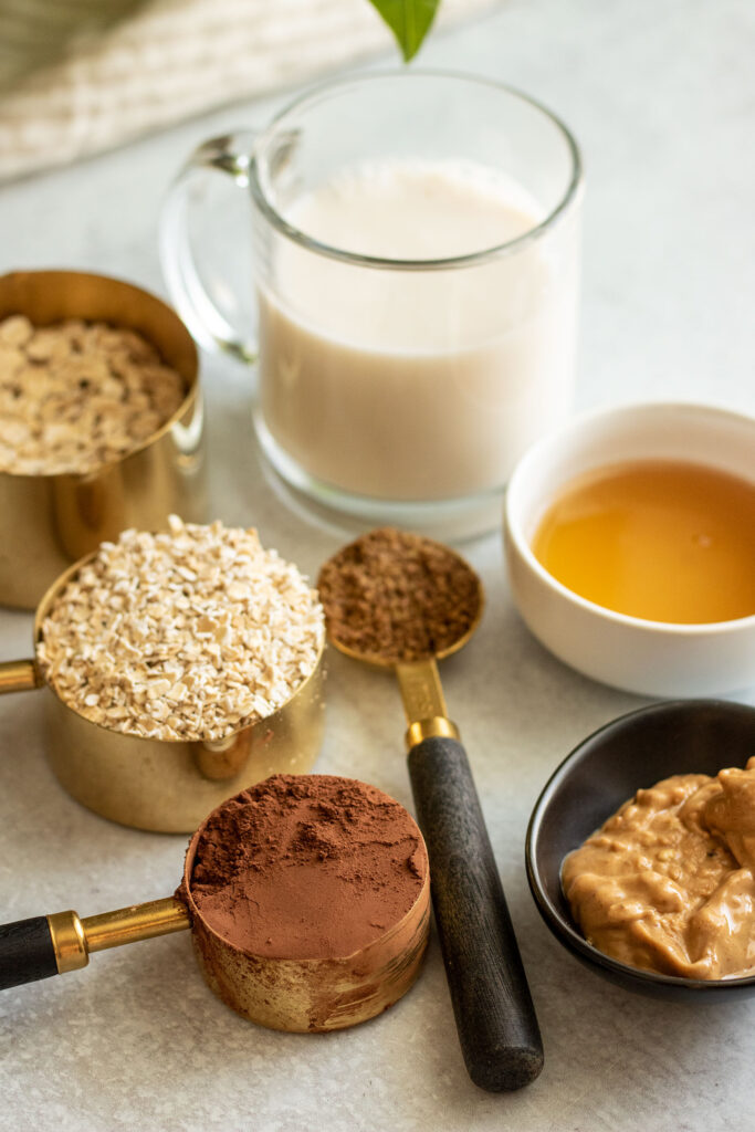 Showing all 7 ingredients needed to make this bowl including cocoa powder, oats, milk, maple syrup, flaxseed and peanut butter.