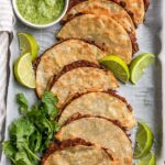 Chipotle black bean stuffed tacos arranged on a baking tray with lime wedges and cilantro.