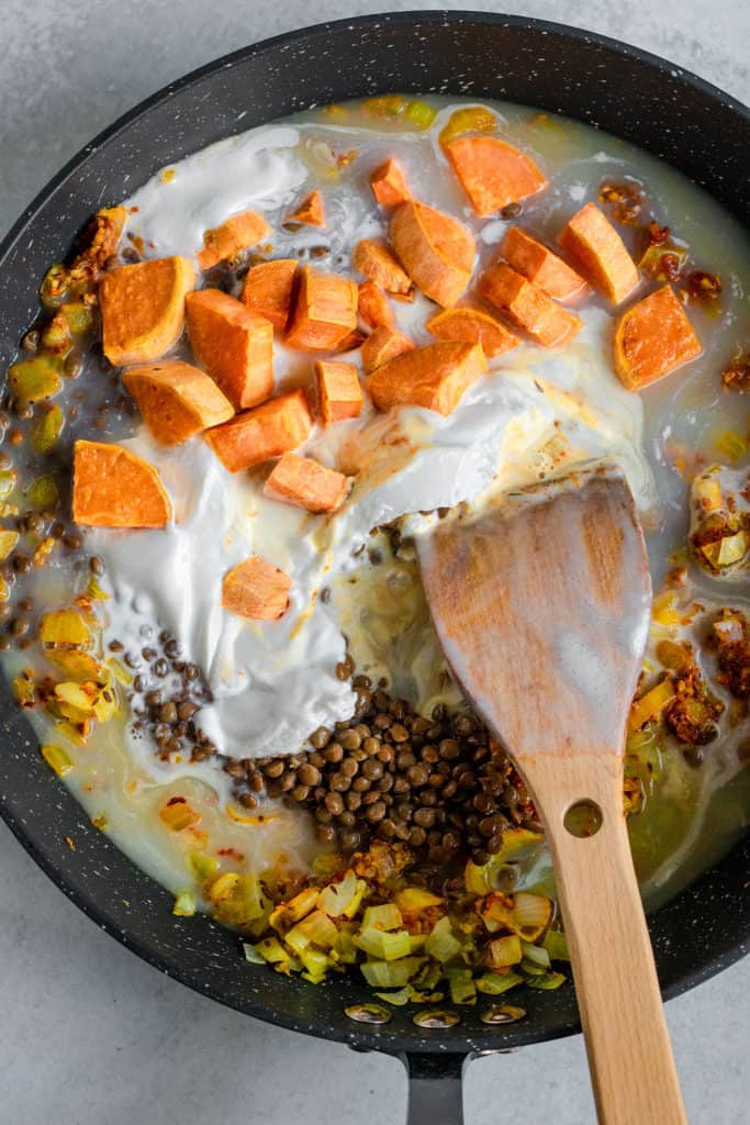 Adding potato, lentils and coconut to the spice mix in the pan.