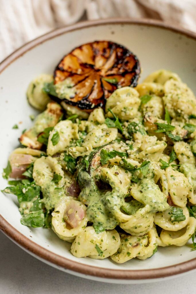 Side view of a bowl of lemon basil pasta salad served with seared lemon and topped with hemp hearts.