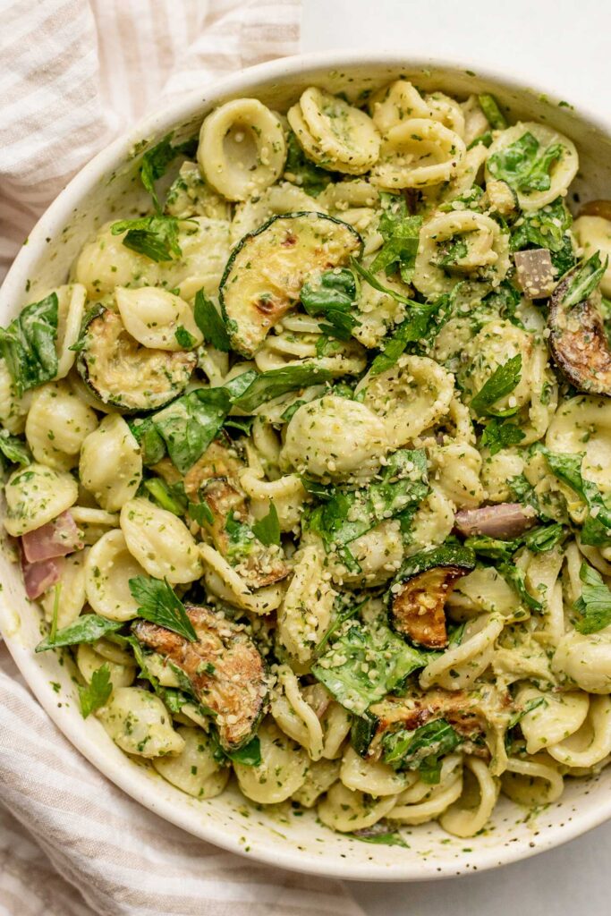 Large bowl of lemon basil pasta mixed with seared zucchini and onions and topped with hemp hearts.