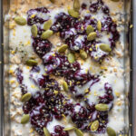 Preparing the overnight oats in a breakfast box container and topping with blueberry jam, yogurt and pepitas.
