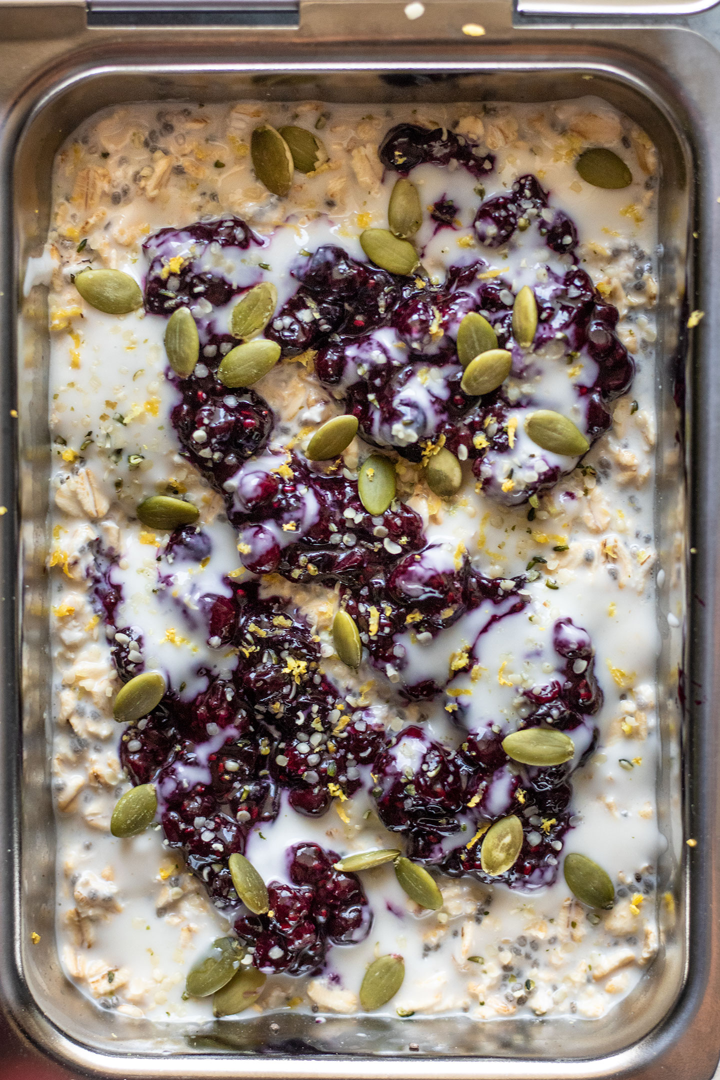 Preparing the overnight oats in a breakfast box container and topping with blueberry jam, yogurt and pepitas.