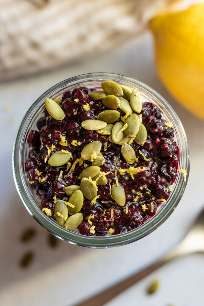 Top down view of a jar of overnight oats topped with blueberry jam, pepitas, and lemon zest.