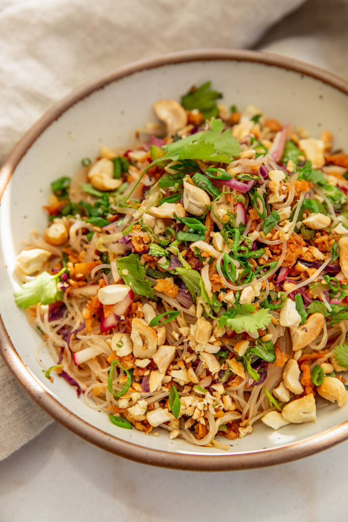 Side view of a bowl with noodles mixed with roasted cabbage and thinly sliced radishes and herbs mixed together.