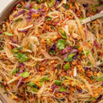 Bowl of noodle salad mixed with roasted cabbage, herbs, jalapeno, roasted cashews and shredded tofu.