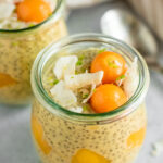 Close up side view of chia pudding mixed with mango and topped with coconut flakes, golden berries and lime zest.
