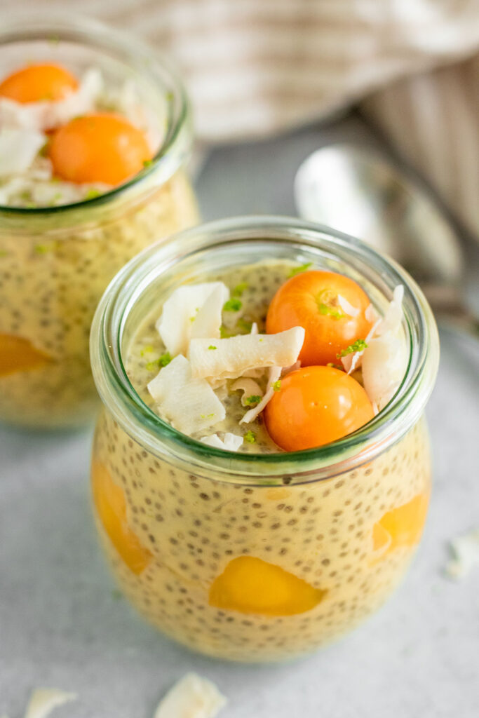 Close up side view of chia pudding mixed with mango and topped with coconut flakes, golden berries and lime zest.