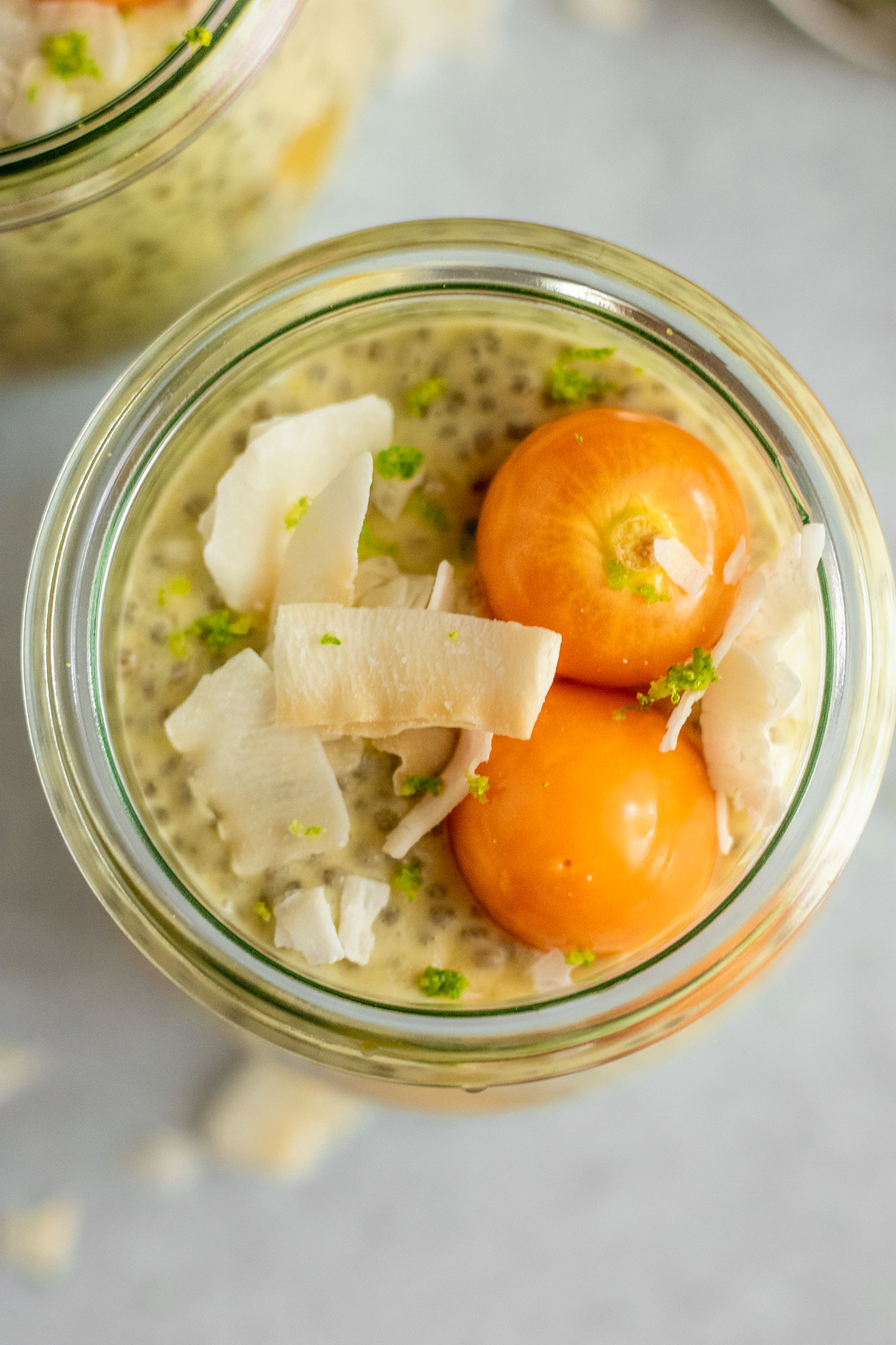 Top down view of a jar of mango chia pudding topped with golden berries, coconut flakes and lime zest.