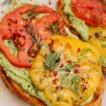 Close up off a piece of toast topped with edamame spread and marinated tomato slices.