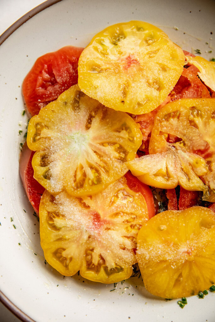 Marinated heirloom tomatoes in a shallow bowl with garlic, lime and dill.