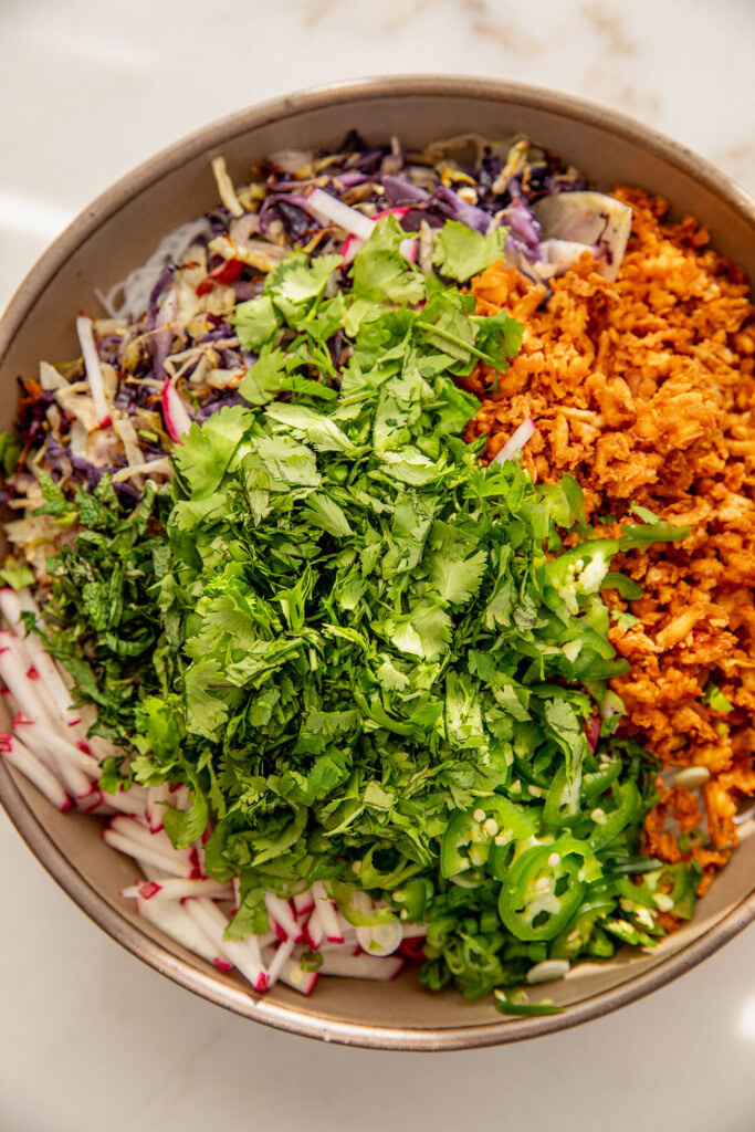 Giant mixing bowl with noodles, shredded tofu and cabbage, herbs, and radishes.