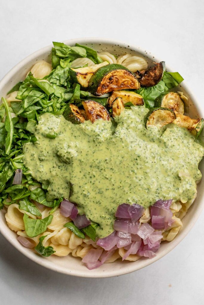 Bowl filled with pasta, zucchini, spinach, onion, and lemon basil sauce.
