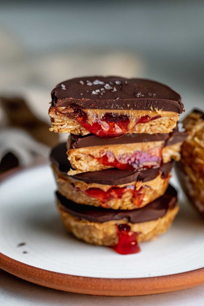 Peanut butter jelly cups stacked together on a plate with the cup on top cut in half to reveal the peanut butter and jelly center.