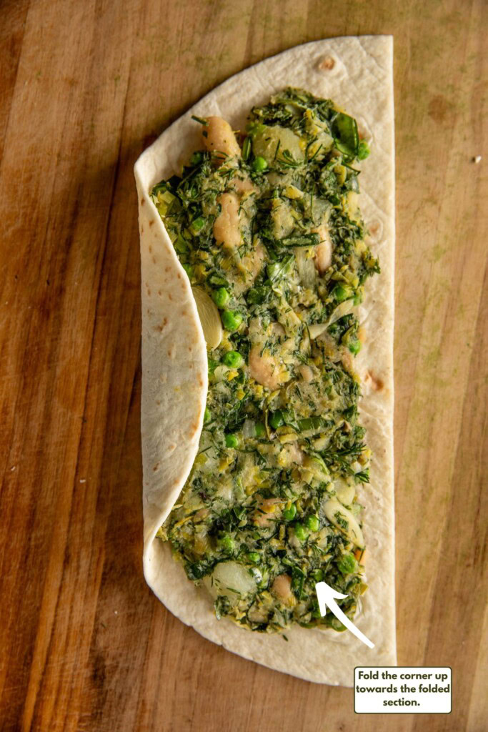 Folding the round edge of the wrap up and over the filling.