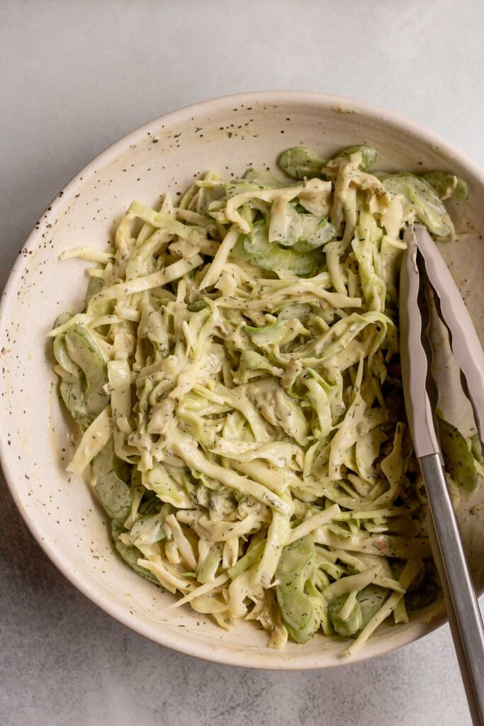 Mixing the cabbage and celery together with a tahini ranch sauce in a bowl with tongs.