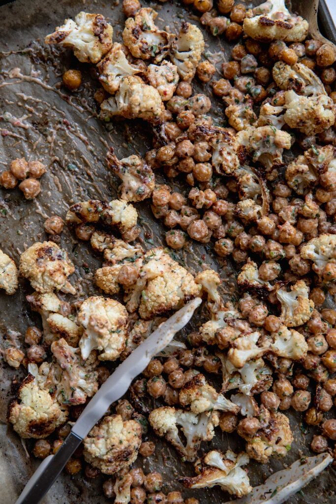 Tossing together charred cauliflower and chickpeas with chipotle sauce on a baking tray.