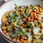 Side view of crispy roasted brussels sprouts and squash topped with crispy chickpeas and herby dressing.