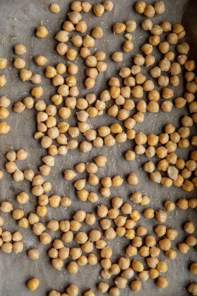 Chickpeas coated with oil on a baking tray.