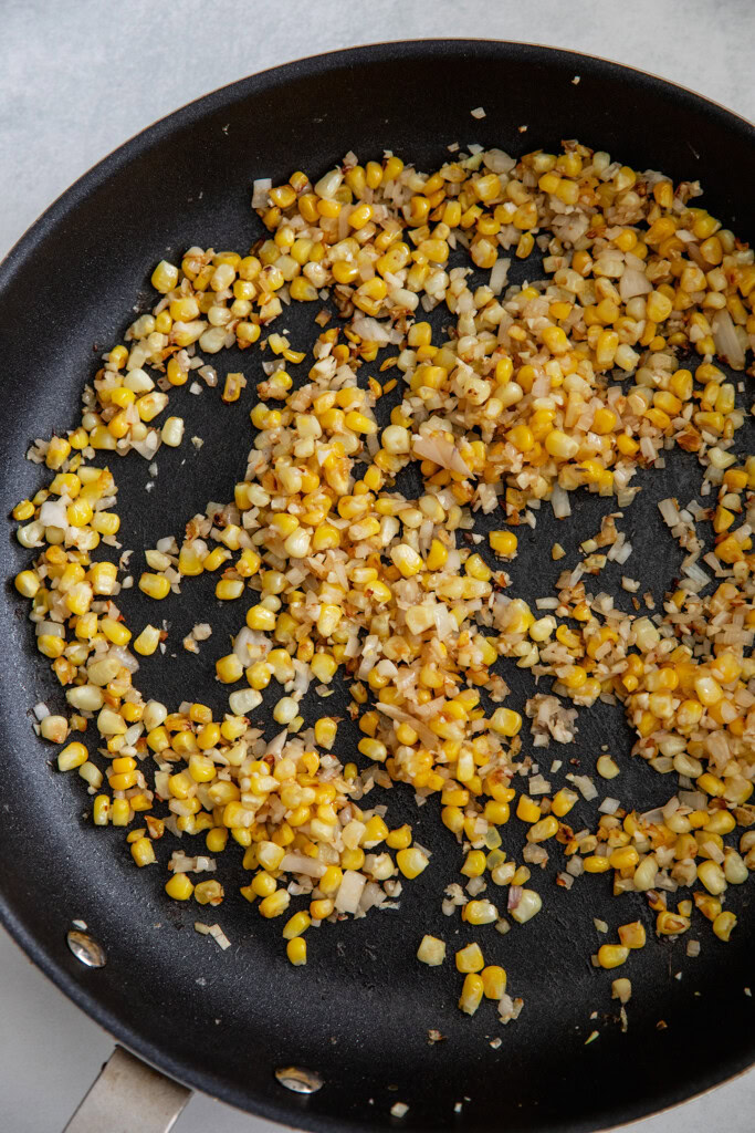 Sautéed corn and shallots in a pan.