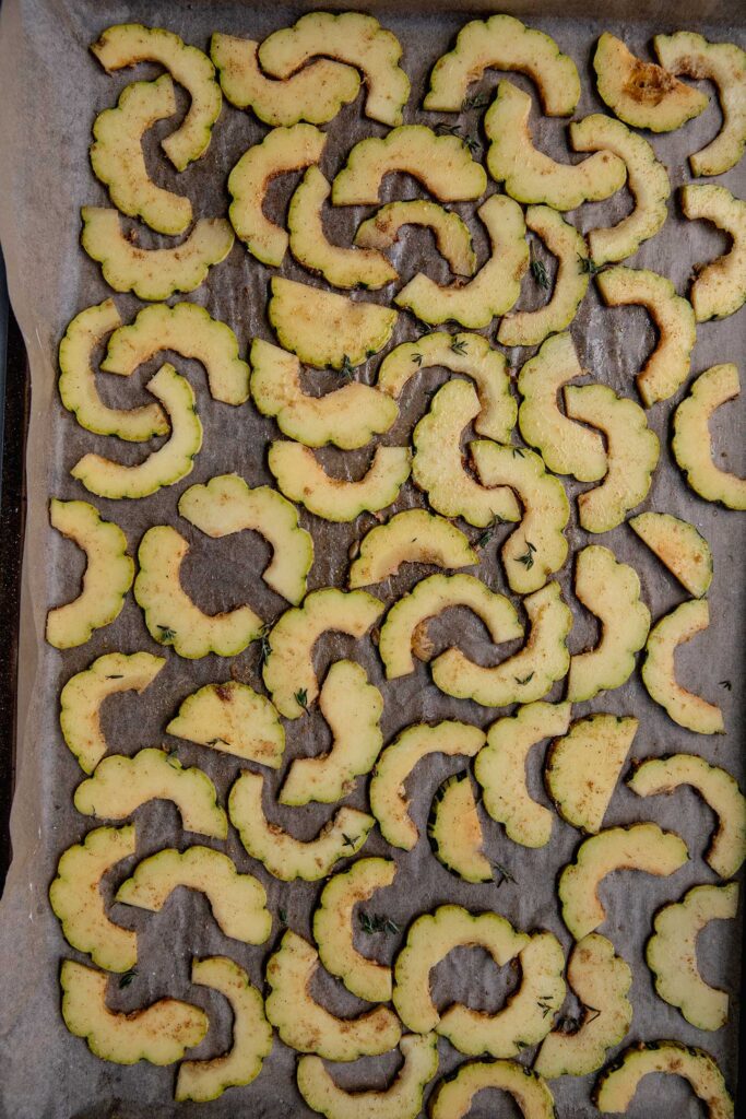 Seasoned delicata squash on a baking tray.