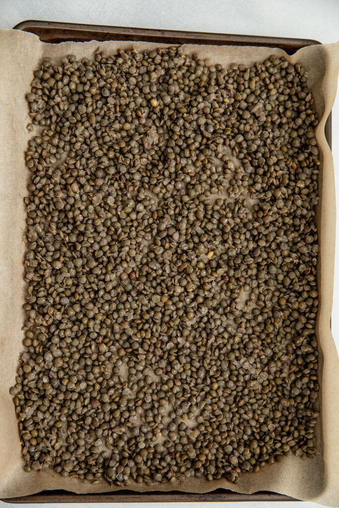 Seasoned lentils on a parchment lined baking tray.