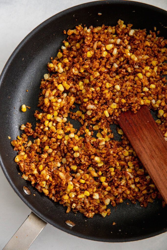 Tempeh hash being mixed in a pan with corn and sauce.