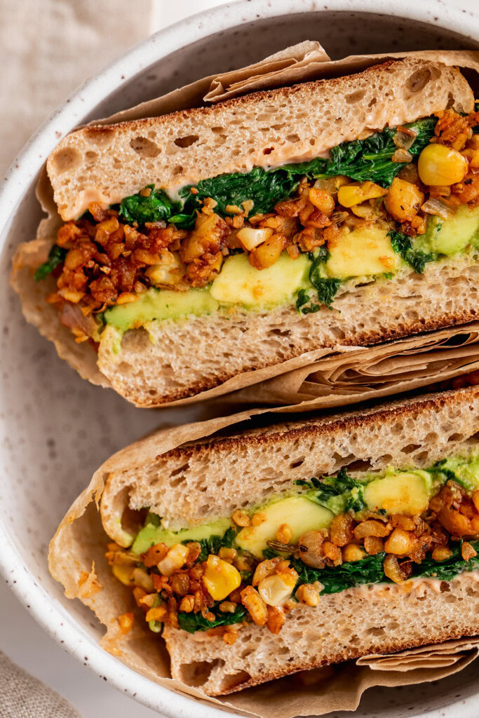 Close up of a breakfast sandwich stuffed with avocado, tempeh and spinach.