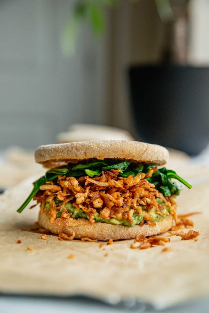 Fully assembled breakfast sandwich in an English muffin layered with avocado, shredded tofu and spinach.