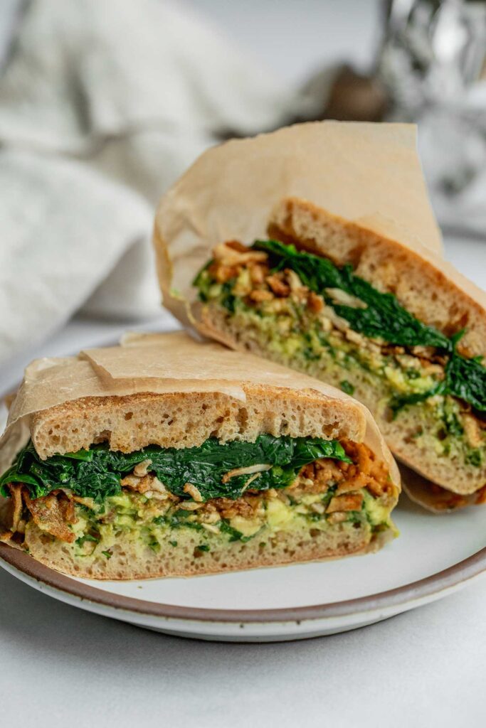 Avocado and shredded tofu breakfast sandwich cut in half on a plate.